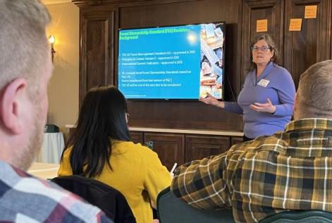 A speaker presents slides about the Forest Stewardship Standard to attendees seated in a meeting room.