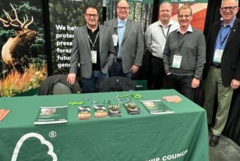 Five people stand behind an FSC display table at a conference booth promoting sustainable forestry.