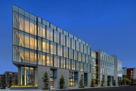 Wide-angle view of glass building glowing against the evening sky.