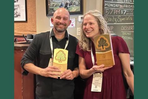 two people smile holding plaques.