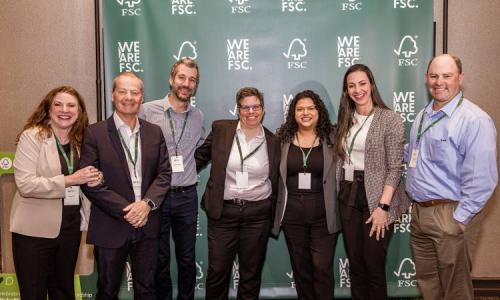 Seven people stand together smiling in front of a "We are FSC" banner.
