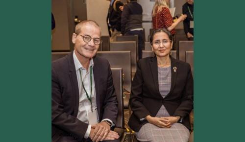 Two people seated and smiling before a conference session begins.