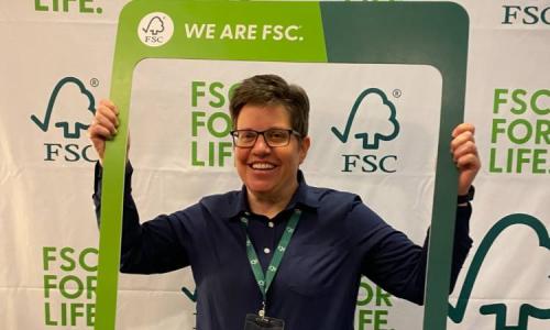Person smiles while holding a “We Are FSC” frame in front of an FSC-branded backdrop.