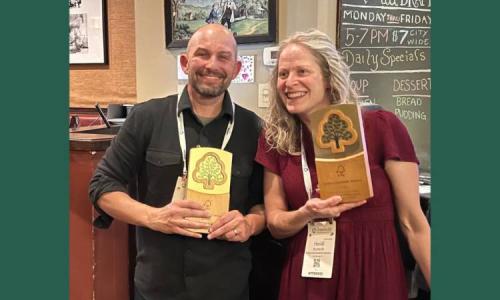 two people smile holding plaques.