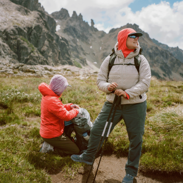 Two backpackers, one sitting one standing, at a scenic, mountain vista.
